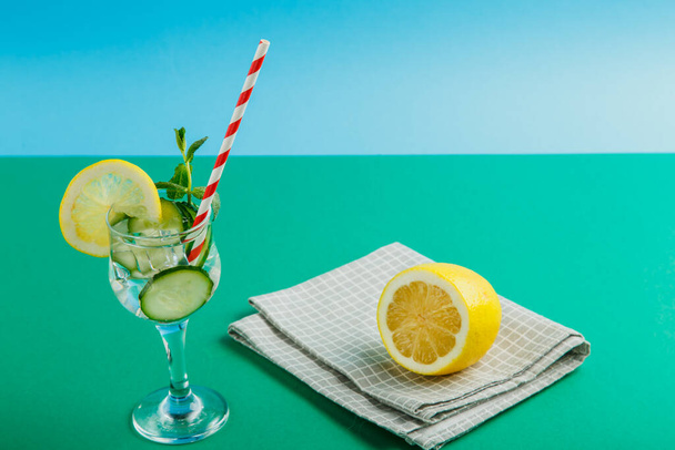 Cocktail cucumber water with lemon and mint in a glass on a napkin on a green background next to a lemon on a napkin. Horizontal photo - Foto, Imagen