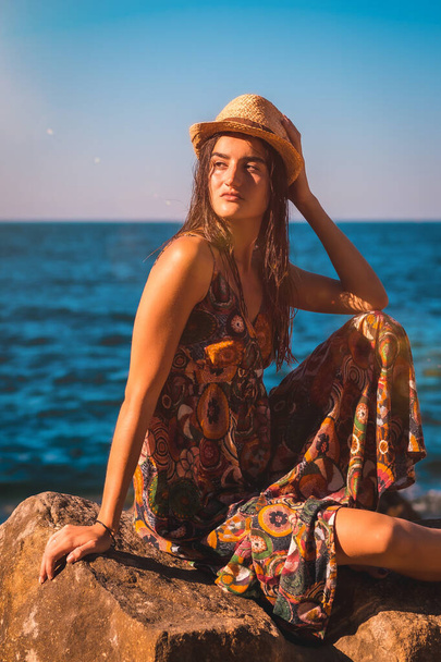 Portrait of a young Caucasian woman with wet hair and a floral dress and a straw hat by the sea, summer lifestyle in the golden hour - Foto, Imagem