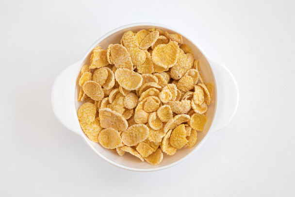 cornflake in schaal op witte achtergrond, bord cornflakes, gezond ontbijtconcept, cornflakes verkruimeld rond de beker, bovenaanzicht - Foto, afbeelding