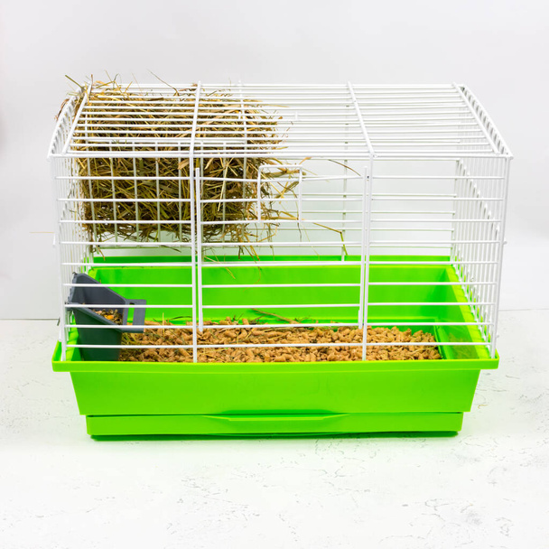 Tierheim mit grüner Palette aus Spänen, Sägemehl, Futter, Heu und Heu. Haustiere in Käfigen halten. Seitenansicht. - Foto, Bild