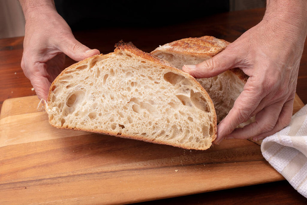 Homemade sourdough bread loaf being sliced on a cutting board by the chef, after being baked in the oven - Foto, Imagen