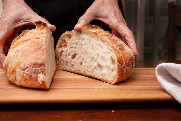 Homemade sourdough bread loaf being sliced on a cutting board by the chef, after being baked in the oven - Photo, Image