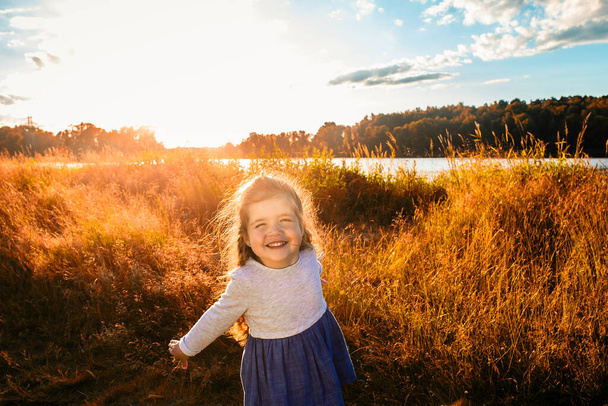 glückliches kleines Mädchen läuft durch ein Feld in der Natur, in den Strahlen des Sonnenuntergangs. - Foto, Bild