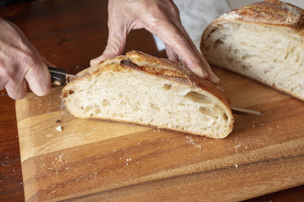 Homemade sourdough bread loaf being sliced on a cutting board by the chef, after being baked in the oven - Foto, Imagen