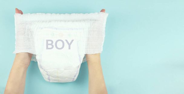 Baby diaper on hand with inscription BOY, on blue background. Space for text. - Zdjęcie, obraz