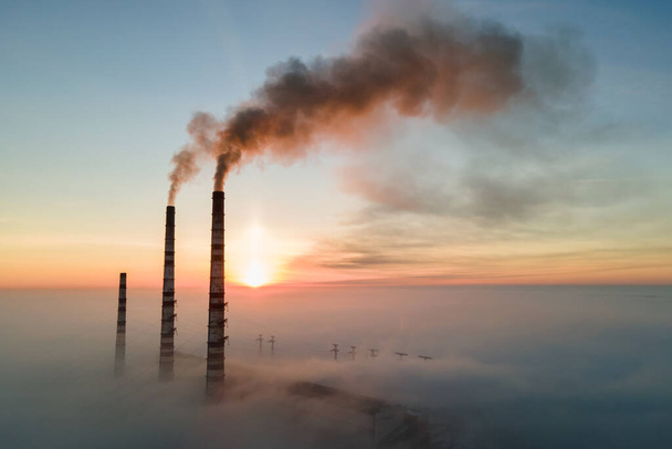 Vista aérea de las altas tuberías de las centrales eléctricas de carbón con humo negro subiendo por la atmósfera contaminante al atardecer. - Foto, imagen
