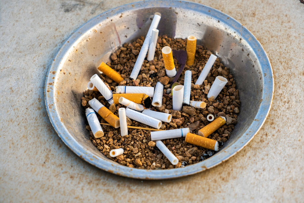 Zamknij niedopałki papierosów w metalowej popielniczce na ulicy. Pojęcie wielu szczątków papierosów po paleniu. - Zdjęcie, obraz