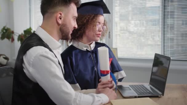 friendly support, happy female student in an academic mantle and hat received her diploma online during distance education and hugs man - Video