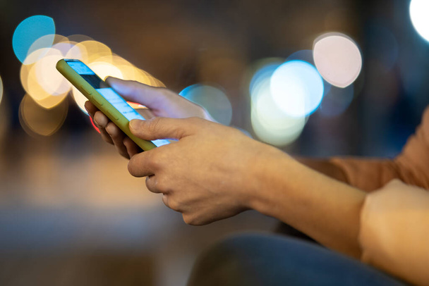 携帯電話を持っている女性の手の閉鎖夜にぼやけた光と街の通りでインターネットを閲覧. - 写真・画像