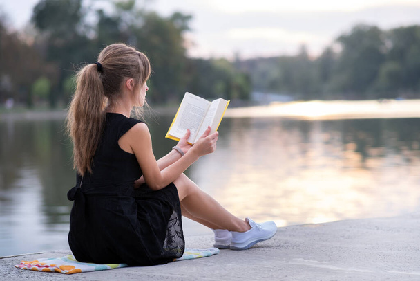 Νεαρή γυναίκα ξεκουράζεται στο πάρκο διαβάζοντας ένα βιβλίο. Εκπαίδευση και κατάρτιση. - Φωτογραφία, εικόνα