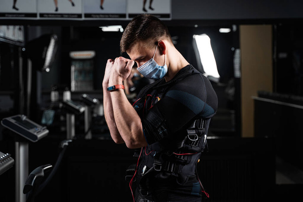 Man in EMS suit and medical mask in gym. Protection from coronavirus covid-19. Sport training in electrical muscle stimulation suit at quarantine period - Foto, Imagem