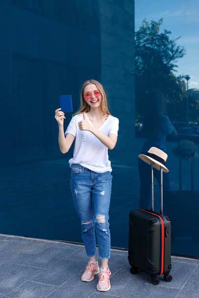 La mujer está contenta con su pasaporte y equipaje en el fondo azul de la terminal. Viaje 2021 - Foto, imagen
