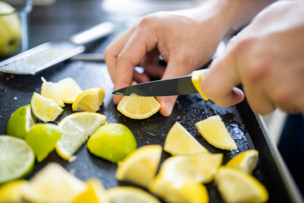 Male hands slicing lemons and limes on a black tray - Photo, Image