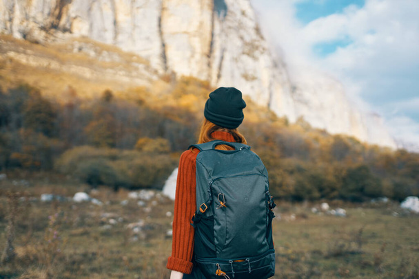 Kobieta w ciepłym kapeluszu z plecakiem na plecach i w swetrze na świeżym powietrzu w górach gestykulować rękami - Zdjęcie, obraz