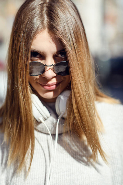 a modern girl with sunglasses walking down the street listens to music in headphones. - Foto, Bild