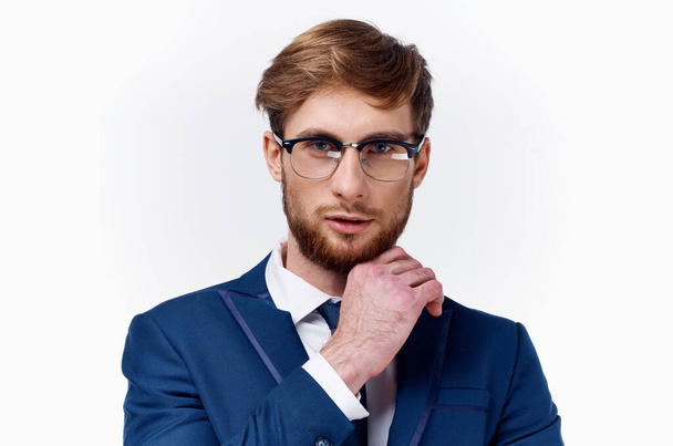 Takım elbiseli ve gözlüklü bir iş adamı açık arkaplan mavi ceket kravat klasiğinde elini yüzüne yakın tutuyor. - Fotoğraf, Görsel