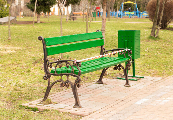 Свежераскрашенная скамейка с предупреждающей лентой стоит в городском парке - Фото, изображение