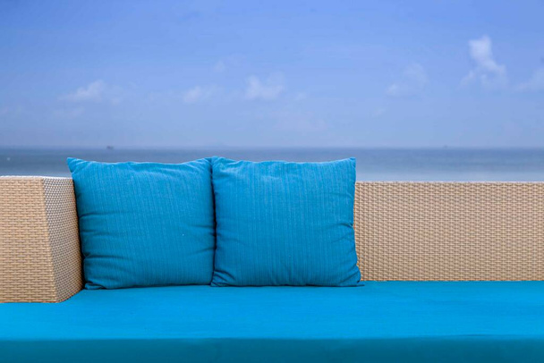 Long brown wicker sofa and blue cushions and cushions placed on the beach - Фото, зображення