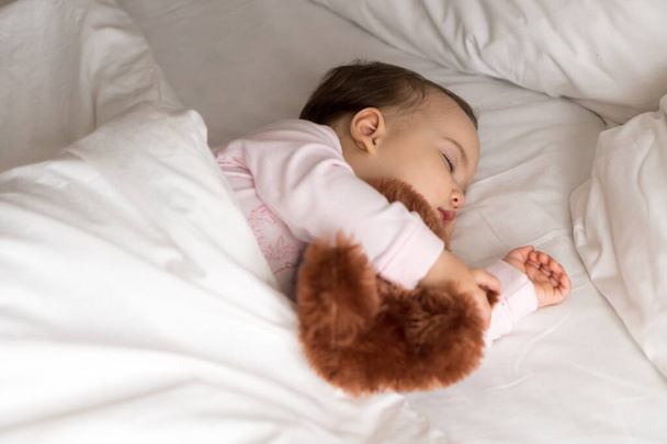 Authentic portrait cute caucasian little infant chubby baby girl or boy in pink sleep with teddy bear on white bed. child resting at lunchtime. care, Sleeping kid, Childhood, Parenthood, life concept - Foto, afbeelding