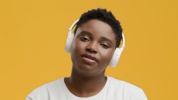 Mujer afroamericana con auriculares escuchando música, fondo amarillo - Imágenes, Vídeo