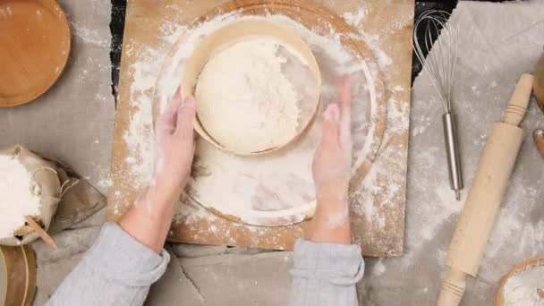 женские руки просеивают белую пшеничную муку через деревянное круглое сито, вид сверху на стол с ингредиентами - Кадры, видео
