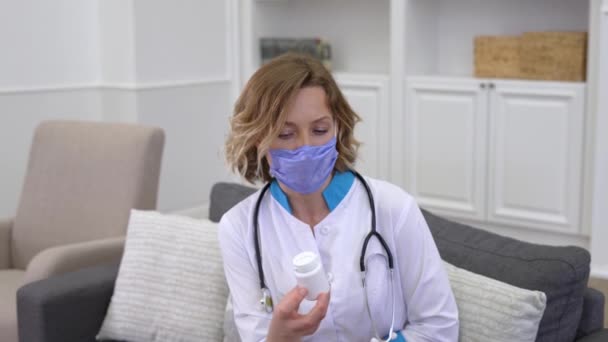 Junge Ärztin mit Schutzmaske verschreibt Patientin bei Hausbesuch Medikamente - Filmmaterial, Video