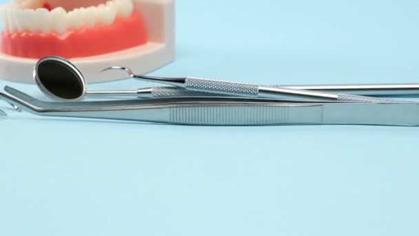 modelo plástico de la mandíbula con dientes blancos y diversos instrumentos dentales para el trabajo del médico en la cavidad oral, fondo azul, movimiento de la cámara de derecha a izquierda - Metraje, vídeo