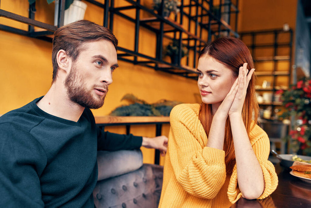 un hombre le dice algo a una mujer joven en un suéter en una mesa en un café interior amigos comunicación - Foto, Imagen