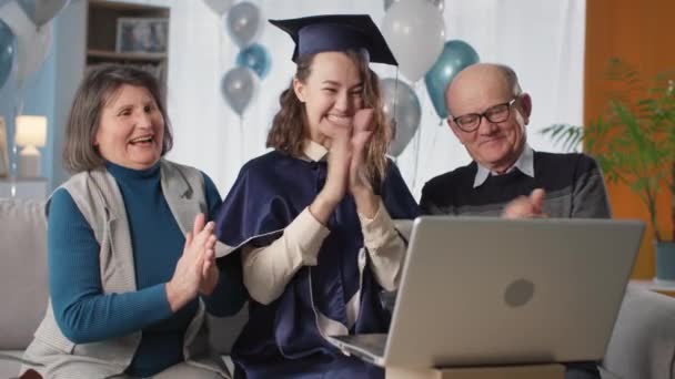 girl in hat and gown, together with parents rejoices at end of universal and clap their hands during a remote greeting to teacher via video link, pandemic - Video