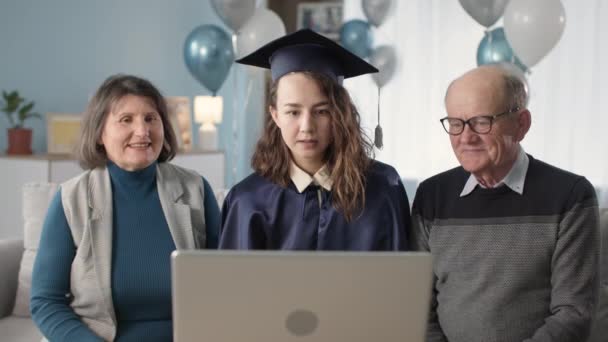 celebration in quarantine, young female student wearing mantle and academic hat along with mom and dad receive diploma online via video link on laptop - Video