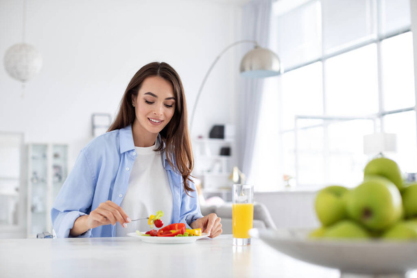 Healthy smiling woman eating wholesome breakfast fresh vegetable salad at the kitchen table at home. - Foto, imagen