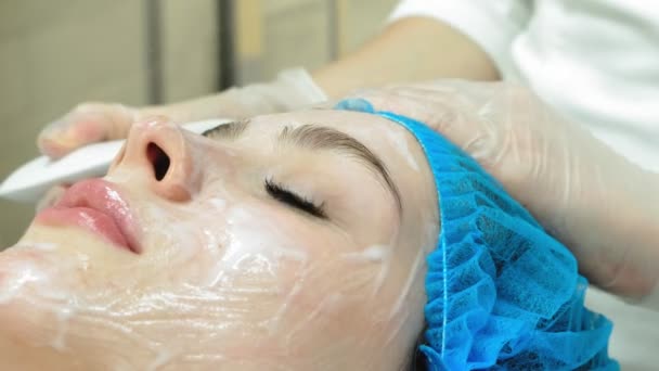 Een vrouwelijke cosmetoloog geeft een jong meisje een gezichtsmassage Een vrouwelijke cosmetoloog geeft een jong meisje een gezichtsmassage close-up van het gezicht - Video