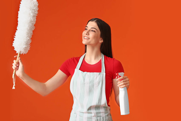 Mujer joven con cepillo de polvo y detergente sobre fondo de color - Foto, imagen