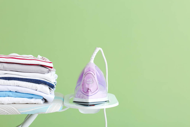 Board with electric iron and clean clothes on color background - Photo, Image