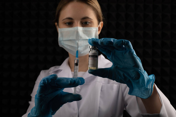 Woman doctor holding covid vaccine and syringe on dark background. - Foto, imagen