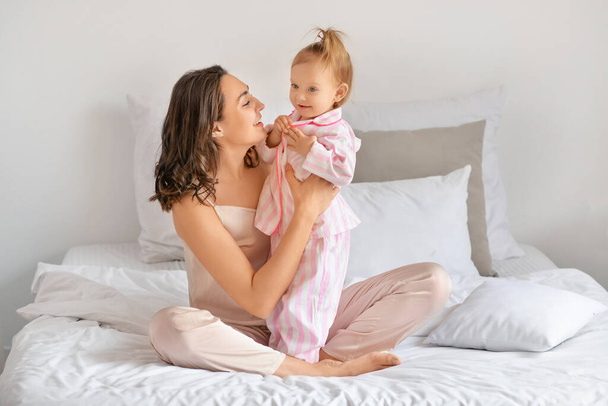 幸せな女性と彼女の小さな娘座っています上のベッドに家 - 写真・画像