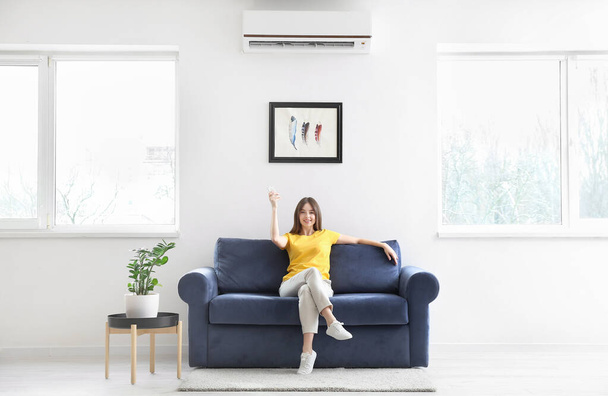 Young woman with air conditioner remote control at home - Photo, image