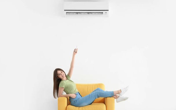 Mujer joven con control remoto de aire acondicionado cerca de la pared blanca - Foto, Imagen