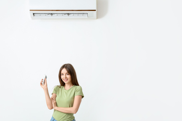 Young woman with air conditioner remote control near white wall - Фото, зображення