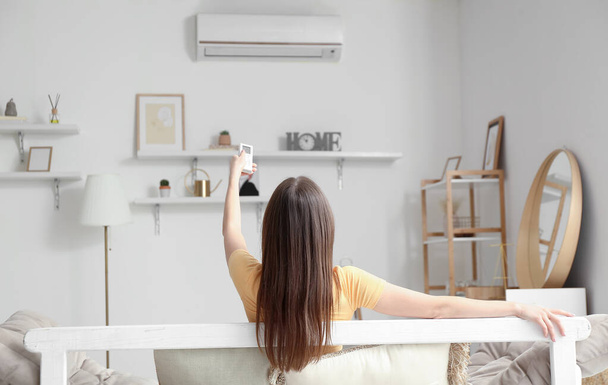 Młoda kobieta z klimatyzatorem zdalnego sterowania na kanapie w domu - Zdjęcie, obraz