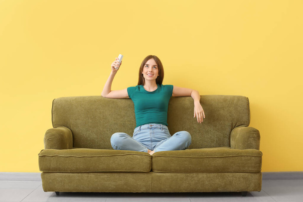 Young woman with air conditioner remote control on sofa near color wall - Photo, Image
