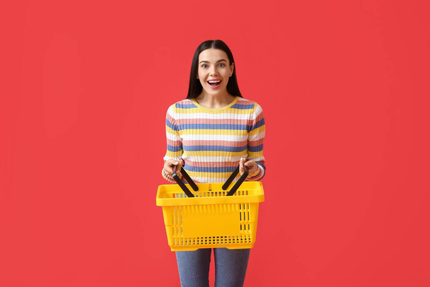色の背景にショッピングバスケットと驚きの若い女性 - 写真・画像