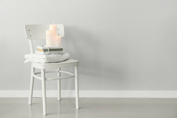 Židle se svetrem, knihami a hořícími svíčkami u světelné stěny - Fotografie, Obrázek