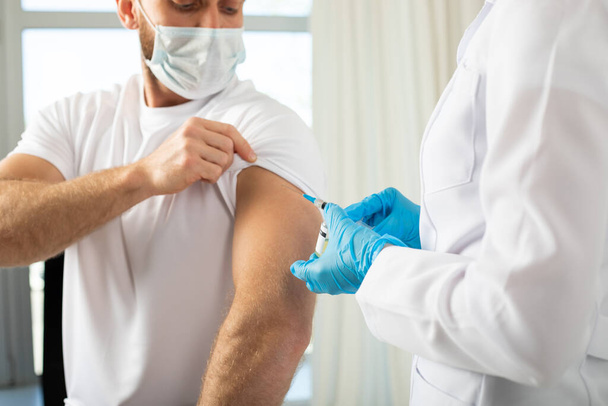 Doctor holding a syringe before injecting coronavirus vaccine into a male patient. - Φωτογραφία, εικόνα