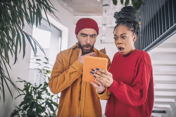 A man in a red hat and a black woman looking surprised whule watching something on a tablet - Fotografie, Obrázek