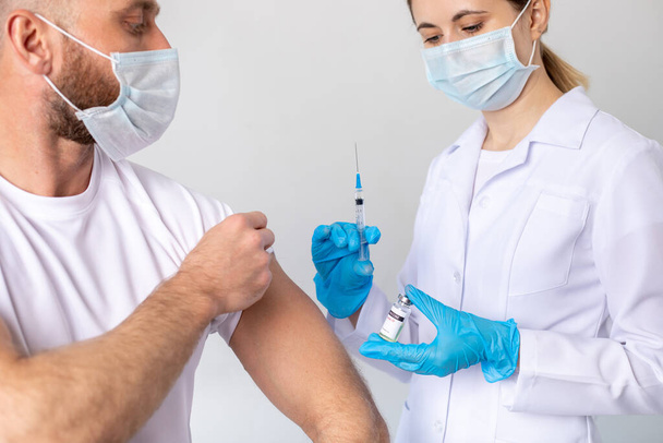 Doctor holding a syringe before injecting coronavirus vaccine into a male patient. - Photo, image
