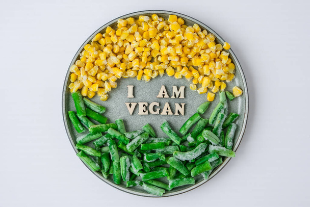 Olen VEGAN teksti lautasella. Vegaani, kasvissyöjä terveellistä elämäntapaa vihreitä papuja keltainen maissi. Terveellinen syöminen vegaani. Puiset kirjaimet - Valokuva, kuva
