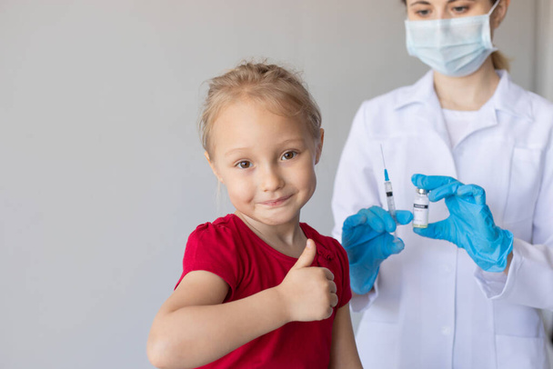 Woman doctor with coronavirus vaccine and child showing thumb up. - 写真・画像