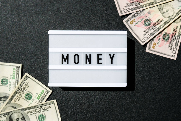 Valolaatikko, jossa lukee "Raha" mustissa kirjaimissa dollarien seteleissä. Rahoituksen tausta. Liiketoiminta, taloudellinen menestys ja rahan tekeminen käsite. Varallisuuden ja vaurauden yritysbudjetti rahoitus. USD dollareita Cash Bill - Valokuva, kuva