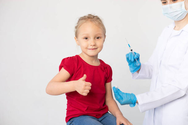 Woman doctor with a syringe and child showing thumb up. - Foto, Bild